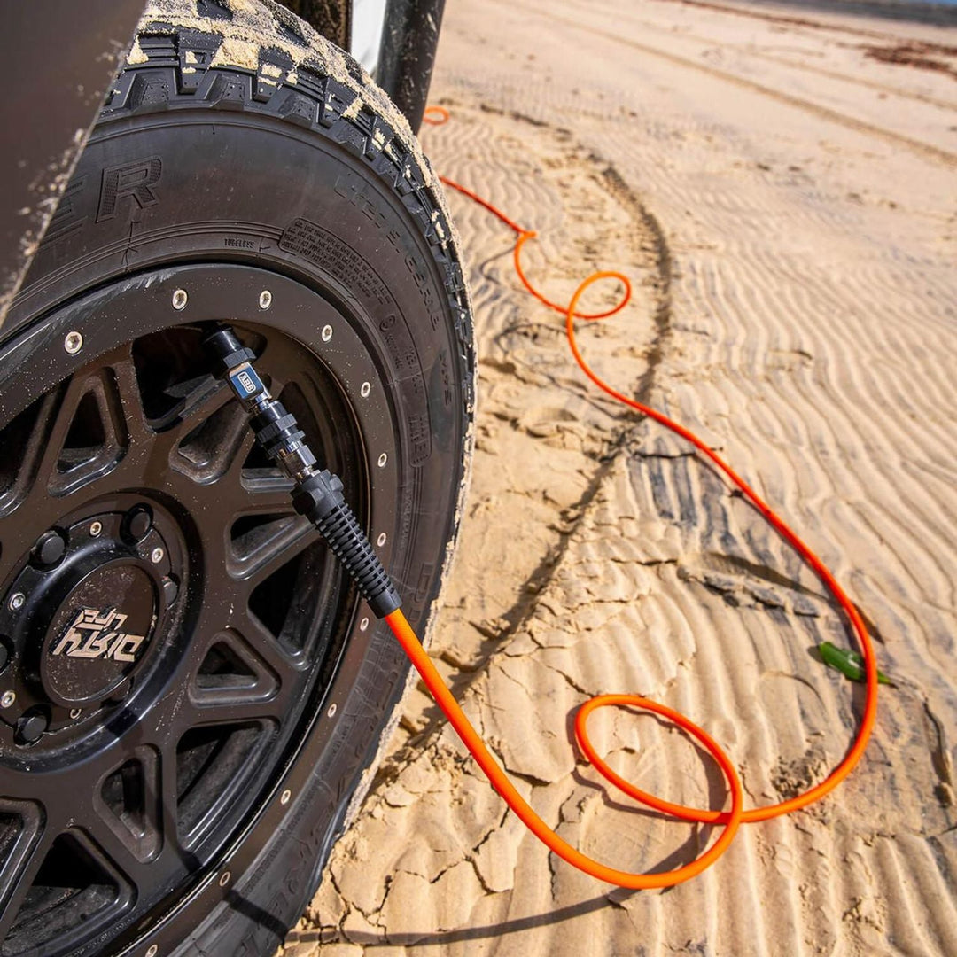 Tire with a black rim and orange off road air compressor hose inflation kit
on sandy terrain