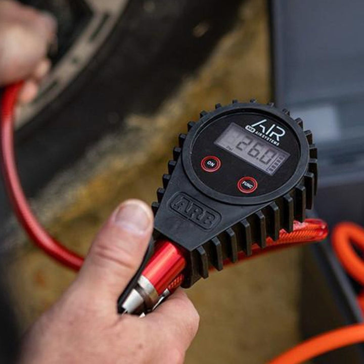 digital air pressure gauge with inflator with digital display held by a hand, with a blurred background of a car.