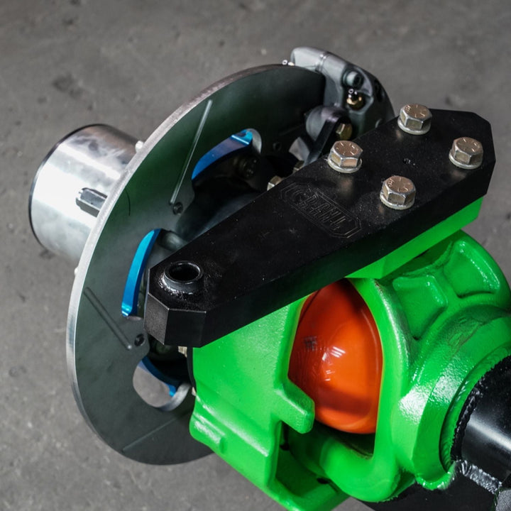 Close-up of a Magnum knuckle 4 piston brake upgrade on a green, orange, and black axle on a gray background